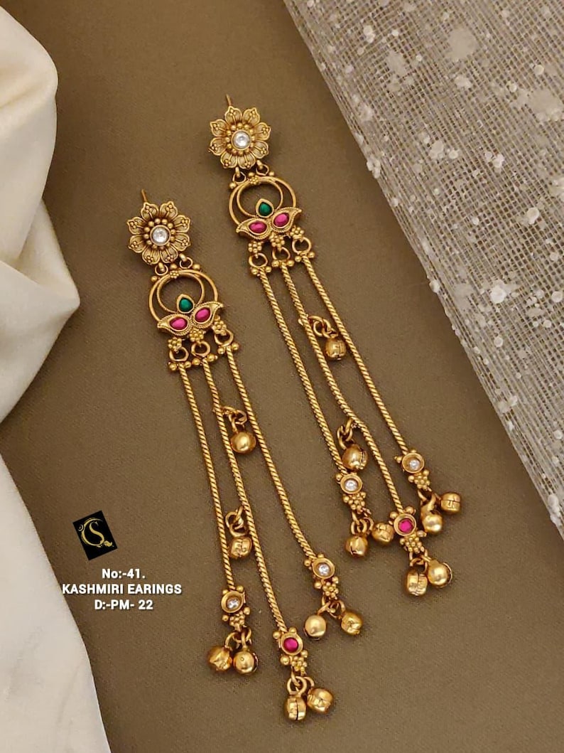 May include: Gold-toned Kashmiri earrings with floral and dangling elements. The earrings feature red and green accents, small clear stones, and a delicate chain design. The earrings have a drop length of approximately 5 inches.