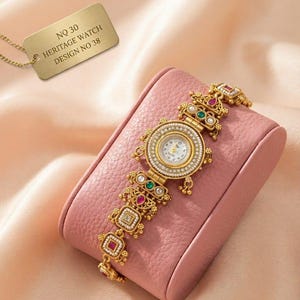 Puede incluir: Un reloj dorado con esfera blanca redonda rodeada de pequeñas cuentas blancas. La correa presenta eslabones dorados ornamentados con pequeñas piedras rojas y verdes y perlas blancas. Una etiqueta dorada muestra el texto NO 30 HERITAGE WATCH DESIGN NO 38.
