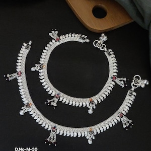 May include: Two white metal silver designer payals, each approximately 25 cm in length, are displayed on a black surface. The payals feature intricate designs with small, colourful accents. The text on the image reads "D.No-M-30 White Metal Silver Designer Payal Size. 10" No.30".