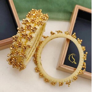 May include: Four gold bangles with a beaded design. The bangles are 2.2, 2.4, 2.6, 2.8, and 2.10 inches in diameter. The text "No:-29. 4-Pis Chudi 2.2/2.4/2.6/2.8/2.10/" is printed below the bangles.