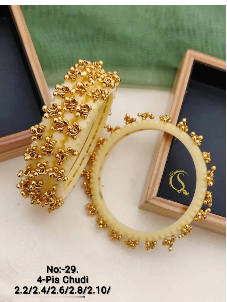 May include: Four gold bangles with a beaded design. The bangles are 2.2, 2.4, 2.6, 2.8, and 2.10 inches in diameter. The text "No:-29. 4-Pis Chudi 2.2/2.4/2.6/2.8/2.10/" is printed below the bangles.