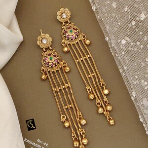 May include: Gold-toned Kashmiri earrings with floral and circular designs. The earrings feature red and green gemstones, dangling chains, and small gold beads. The text on the image reads "Kashmiri Earrings".