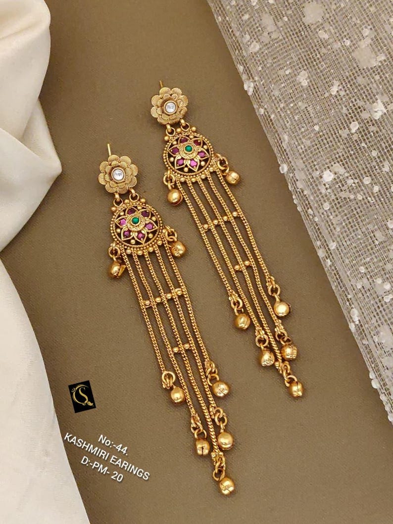 May include: Gold-toned Kashmiri earrings with floral and circular designs. The earrings feature red and green gemstones, dangling chains, and small gold beads. The text on the image reads "Kashmiri Earrings".