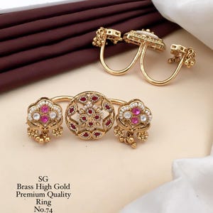 Op de afbeelding: Twee goudkleurige messing dubbele vingerringen met ingewikkeld filigraan metaalwerk, kleine witte kralen en ingebedde rode en roze stenen. De tekst SG Brass High Gold Premium Quality Ring No.74 staat in het zwart linksonder afgedrukt.