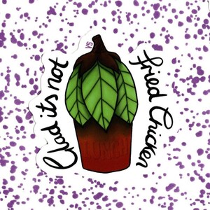 May include: A sticker with a white background and purple splatter paint. The sticker features a cartoon illustration of a green plant in a red pot with the text "Glad it's not Fried Chicken" written around it.