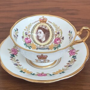 Op de afbeelding: Een wit theekopje en schotel met een gouden rand. Het theekopje heeft een portret van koningin Elizabeth II en de tekst "June 2nd 1953 Coronation" en "E.R.". De schotel heeft een bloemmotief.