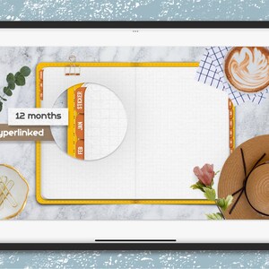 K&ouml;nnte beinhalten: Ein digitaler Planer mit gelbem Einband und einer wei&szlig;en, karierten Seite. Der Planer hat Registerkarten f&uuml;r jeden Monat, beschriftet mit "Jan" bis "Dez". Der Planer ist auf einer leeren Seite ge&ouml;ffnet. Das Bild zeigt au&szlig;erdem eine Tasse Kaffee, einen Strohhut und eine Blume.