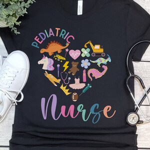 May include: Black t-shirt with a colourful heart design featuring various children's toys and the text "Pediatric Nurse".