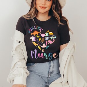 May include: A black t-shirt featuring a colourful heart design that reads "Pediatric Nurse". The heart is filled with various icons associated with children, such as a dinosaur, a unicorn, a teddy bear, a stethoscope, a crown, and a toy truck.