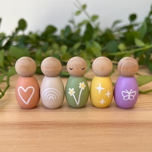 May include: Five wooden peg dolls with painted designs. The dolls are painted in peach, cream, green, yellow, and purple. Each doll features a different design, including a heart, rainbow, flowers, stars, and a butterfly.