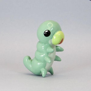 Peut inclure: Figurine de chenille vert clair avec un corps segmenté, des yeux noirs et un nez jaune et rouge. La sculpture en pâte polymère faite à la main a de petites pattes et est posée debout. Le logo Delta Craft est dans le coin supérieur droit.