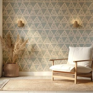 Può includere: Una stanza luminosa con una palette di colori neutri. Una poltrona in legno con un cuscino color crema è appoggiata su un tappeto tessuto. La parete è decorata con un motivo geometrico a triangoli. Un cesto intrecciato contiene piante essiccate.