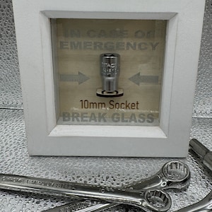 May include: A white wooden frame with a glass panel displaying a 10mm socket and the text "In Case of Emergency 10mm Socket Break Glass".