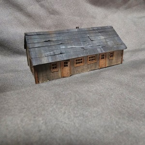 May include: A small wooden model of a building with a weathered gray roof and multiple windows. The building is made of wood and has a rustic appearance.