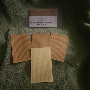 May include: A package of miniature brown and tan adhesive three-tab shingles, with four individual sheets and a package of shingles. The package has text that reads "Sell Adhesive Three Tab Shingles. Covers 20 sq. in."