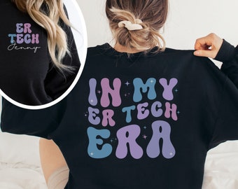 May include: Black sweatshirt with the text "IN MY ER TECH ERA" in a retro font on the back. The front left shoulder has the text "ER TECH Jenny" in a matching font. The text is in shades of blue, purple, and pink.