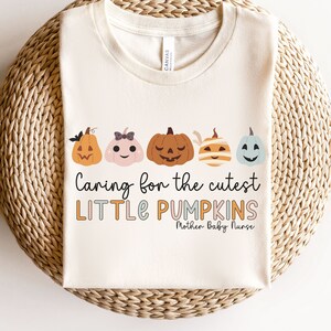 May include: A white t-shirt featuring a graphic of five pumpkins with different faces. The text "Caring for the cutest LITTLE PUMPKINS Mother-Baby Nurse" is printed below the pumpkins.