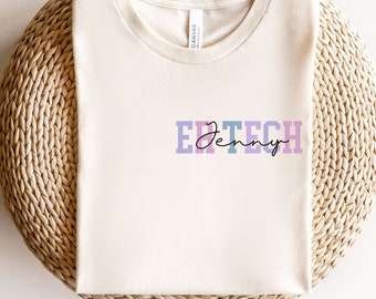 May include: A white t-shirt with the text "ER TECH" in colorful letters and the name "Jenny" written in cursive underneath.