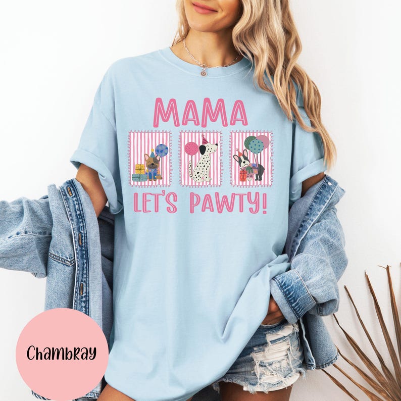 May include: Light blue t-shirt with the word "MAMA" in pink block letters above three framed dog illustrations. The phrase "LET'S PAWTY!" is printed below the illustrations. The shirt features a relaxed fit.