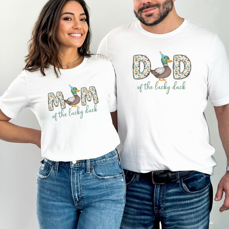 Pode incluir: Duas camisetas brancas com um gr&aacute;fico de pato e o texto "MOM of the lucky duck" e "DAD of the lucky duck".