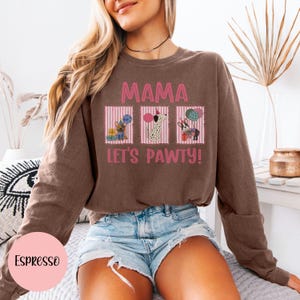 May include: Espresso-colored sweatshirt with the text "MAMA LET'S PAWTY!" and three cartoon dog illustrations. The design includes pink and white striped boxes with dogs holding balloons and gifts. The sweatshirt is a crew neck style.