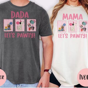 May include: Two t-shirts, one pepper-colored and one ivory-colored, each with a pink graphic. The pepper shirt says "DADA LET'S PAWTY!" and the ivory shirt says "MAMA LET'S PAWTY!". Each shirt features three dog illustrations.