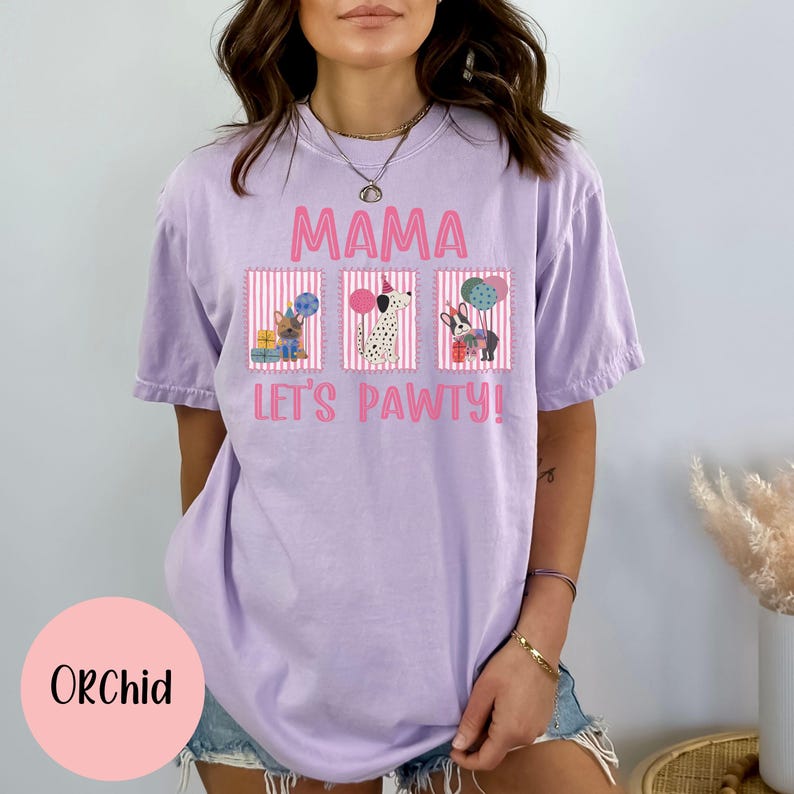 May include: Orchid-colored t-shirt with the text "MAMA LET'S PAWTY!" and three dog illustrations. The illustrations include a French Bulldog, a Dalmatian, and a dog with a gift. The shirt is a relaxed fit.