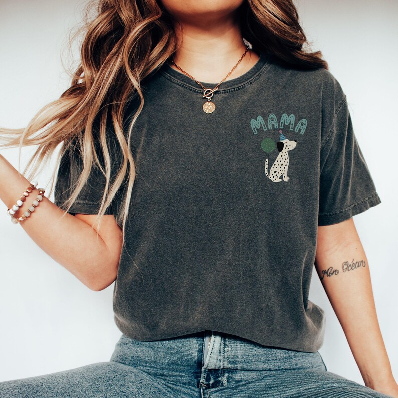 May include: Dark gray t-shirt with the word "MAMA" in teal letters above a Dalmatian dog wearing a party hat and holding a green balloon. The shirt is a relaxed fit.