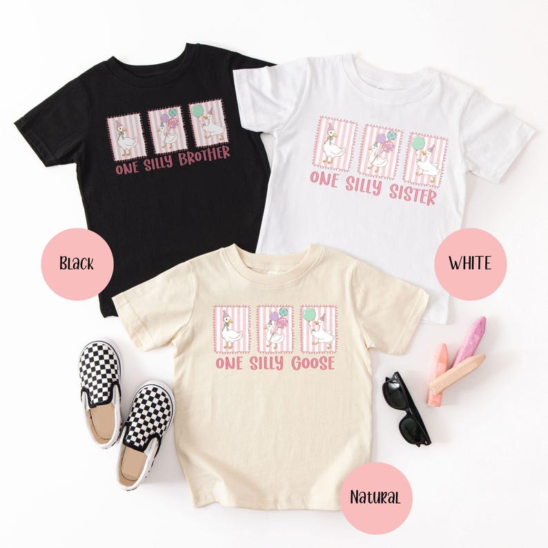May include: Three short-sleeved t-shirts in black, white, and natural colours. Each shirt features a whimsical design of a goose with balloons and the text "ONE SILLY BROTHER", "ONE SILLY SISTER", or "ONE SILLY GOOSE".