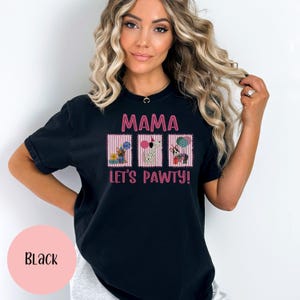 May include: Black t-shirt with the text "MAMA LET'S PAWTY!" in pink. The shirt features three rectangular graphics with cartoon dogs, gifts, and balloons. The shirt is a comfortable, casual style.