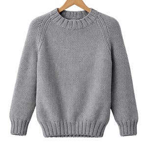 May include: A grey knitted jumper with a crew neck and long sleeves, displayed on a wooden hanger. The jumper features ribbed cuffs, hem, and neckline. The knit pattern is clearly visible throughout the garment.