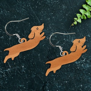 May include: A pair of wooden earrings shaped like a dachshund dog. The earrings are brown and have a silver hook.