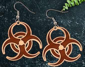 May include: A pair of wooden earrings shaped like biohazard symbols. The earrings are brown and have a silver hook.