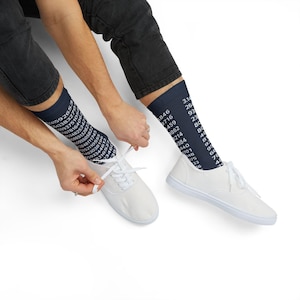 May include: Navy blue socks featuring white numerical data. The socks are worn with white canvas shoes. The person is tying the laces of the shoes. The socks are knee-high.