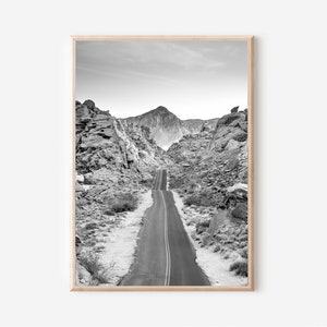 May include: A black and white photograph of a winding road through a desert landscape. The road is lined with rocky hills and mountains in the distance.