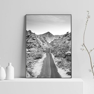 May include: A black and white photograph of a winding road through a rocky mountain landscape.