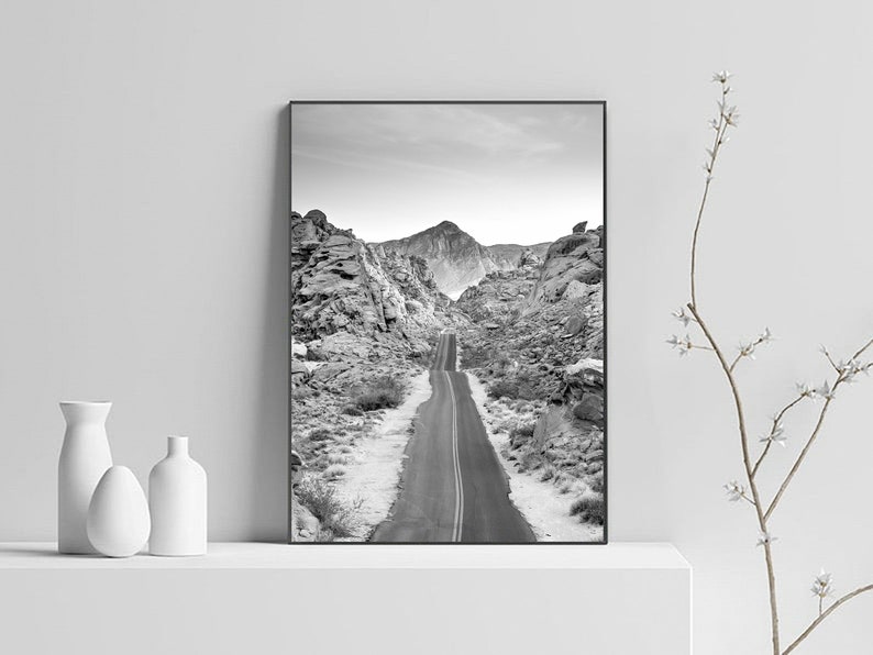 May include: A black and white photograph of a winding road through a rocky mountain landscape.