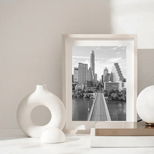 K&ouml;nnte beinhalten: Schwarzwei&szlig;foto einer Skyline mit einer Br&uuml;cke im Vordergrund. Das Foto ist in einem wei&szlig;en Rahmen gerahmt und steht auf einer wei&szlig;en Oberfl&auml;che.