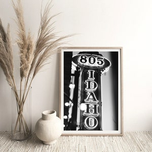 May include: Black and white photograph of a neon sign that reads "IDAHO" with the number "805" above it.