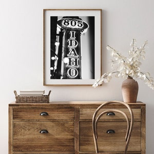 May include: Black and white photograph of a neon sign that reads "805 IDAHO" in a vintage style. The sign is mounted on a building and is illuminated against a dark background.