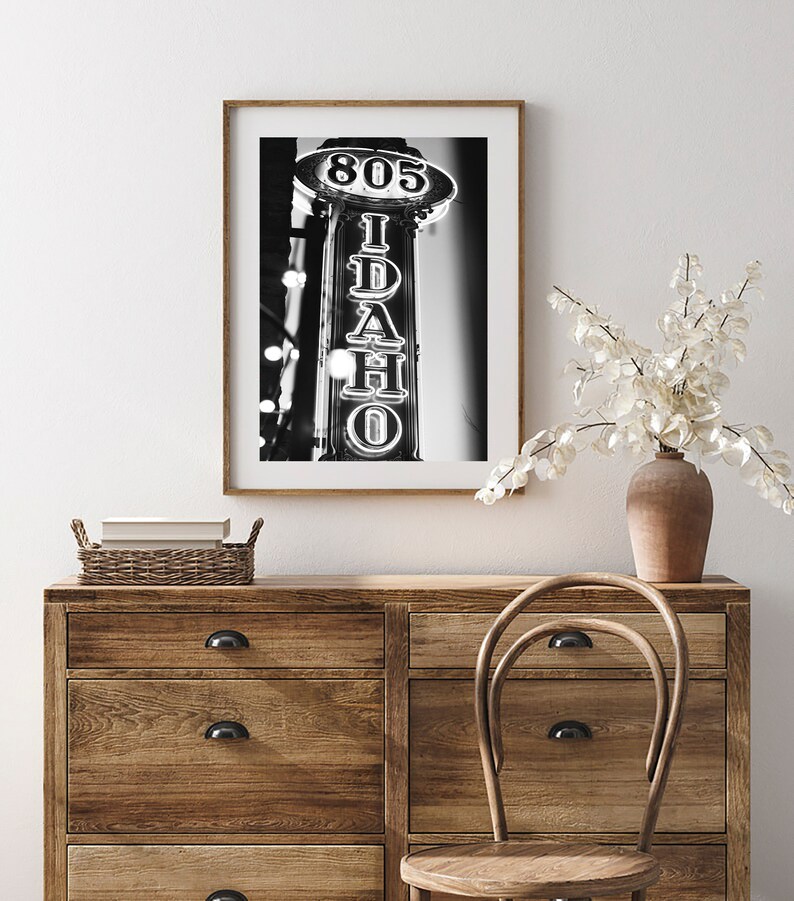 May include: Black and white photograph of a neon sign that reads "805 IDAHO" in a vintage style. The sign is mounted on a building and is illuminated against a dark background.