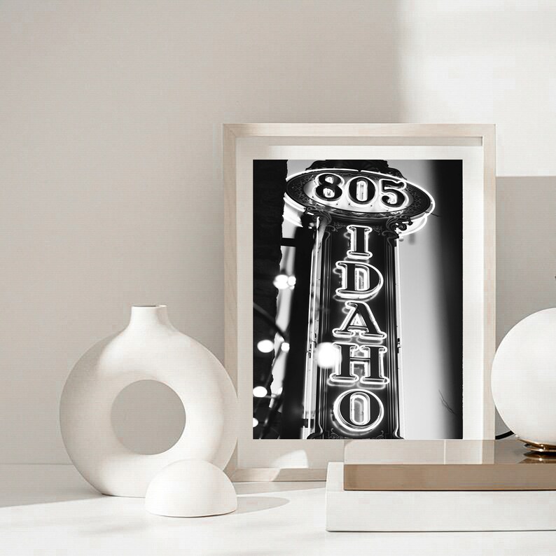May include: Black and white photograph of a neon sign that reads "IDAHO" with the number "805" above it. The sign is on a building in a city.