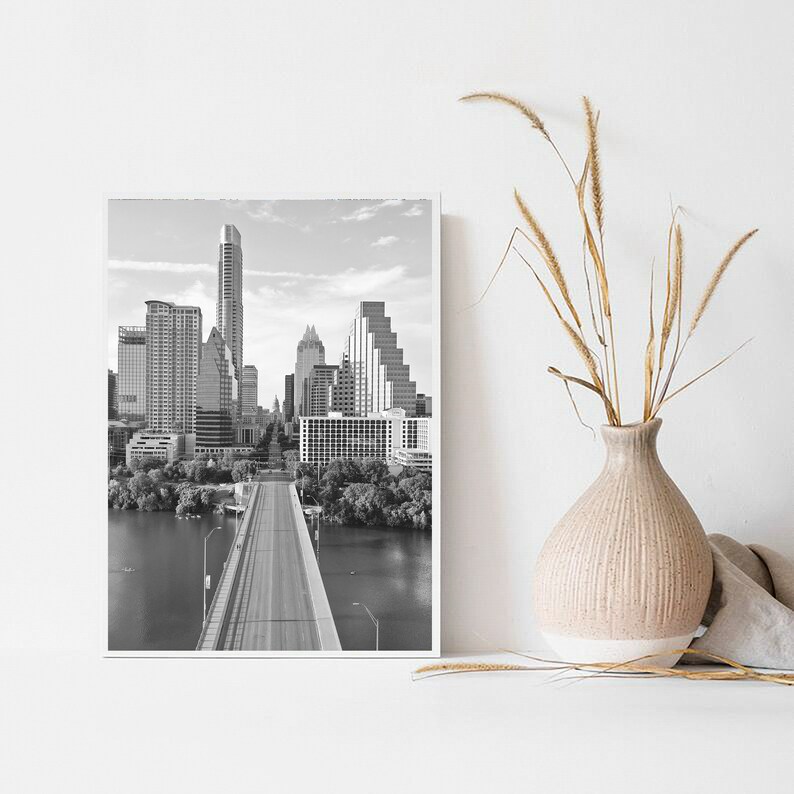 K&ouml;nnte beinhalten: Schwarzwei&szlig;foto der Skyline von Austin, Texas, mit einer Br&uuml;cke, die in die Stadt f&uuml;hrt. Das Foto ist in einem wei&szlig;en Rahmen gerahmt.