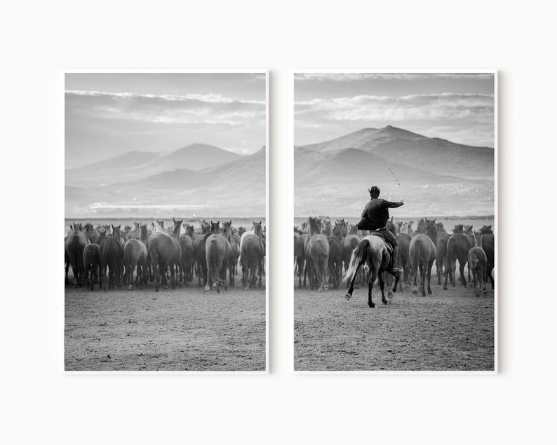 May include: Black and white print of a herd of horses running across a field, with a rider on horseback in pursuit. The background features mountains and a cloudy sky, creating a dramatic landscape scene.