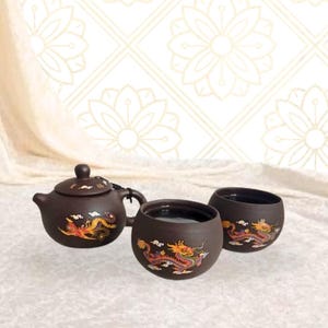 May include: A brown ceramic tea set featuring a teapot with a lid and two matching cups. Each piece is decorated with a colorful dragon design. The set is displayed on a white surface with a patterned background.