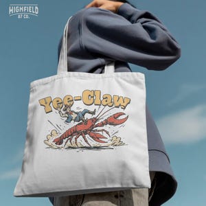 Funny crawdad illustration showing a western cowboy riding a giant crawfish while dust clouds appear under its legs. The Yee Claw phrase adds humor to this Cajun crawfish boil themed design.