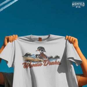 Duck hunting PNG artwork showing a wood duck drake swimming with Woodie Drake wording, outdoor design for hunters
