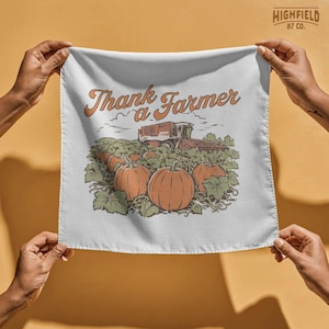 Farmer appreciation shirt design featuring pumpkins in a harvest field with a combine harvester and bold “Thank a Farmer” script in a warm seasonal farm composition.