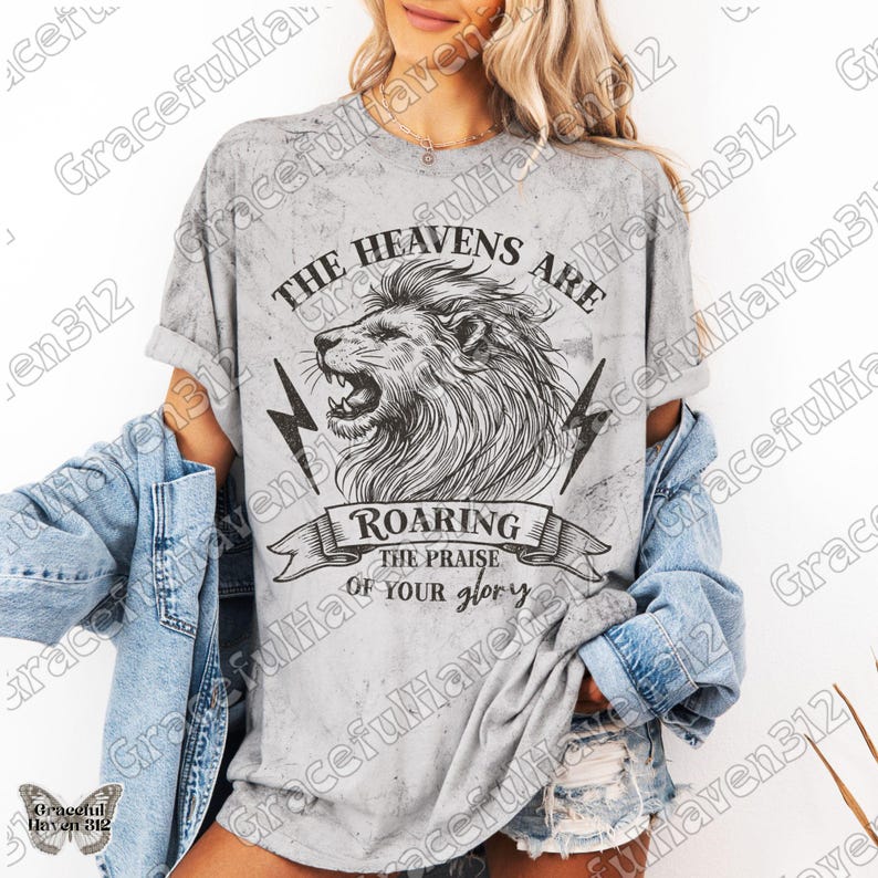 May include: A gray t-shirt with a distressed look featuring a black and white illustration of a lion's head with the text "The Heavens Are Roaring The Praise Of Your Glory".