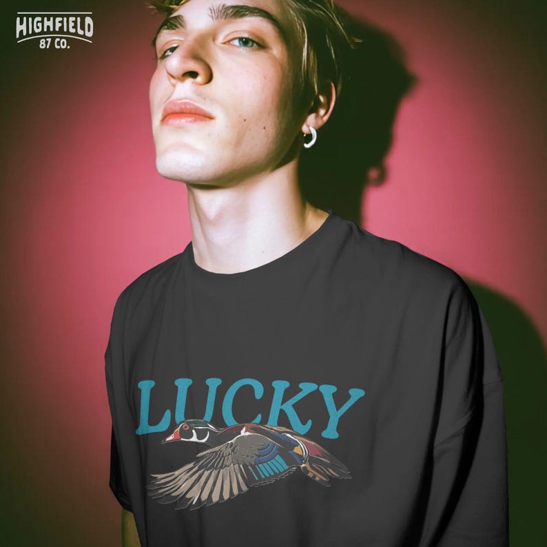 Nature PNG artwork featuring a colorful duck flying in front of large teal Lucky text with detailed feathers and a clean shirt-ready layout. This design is useful for bird lover shirts, outdoor apparel, duck themed gifts, and digital download creative projects.